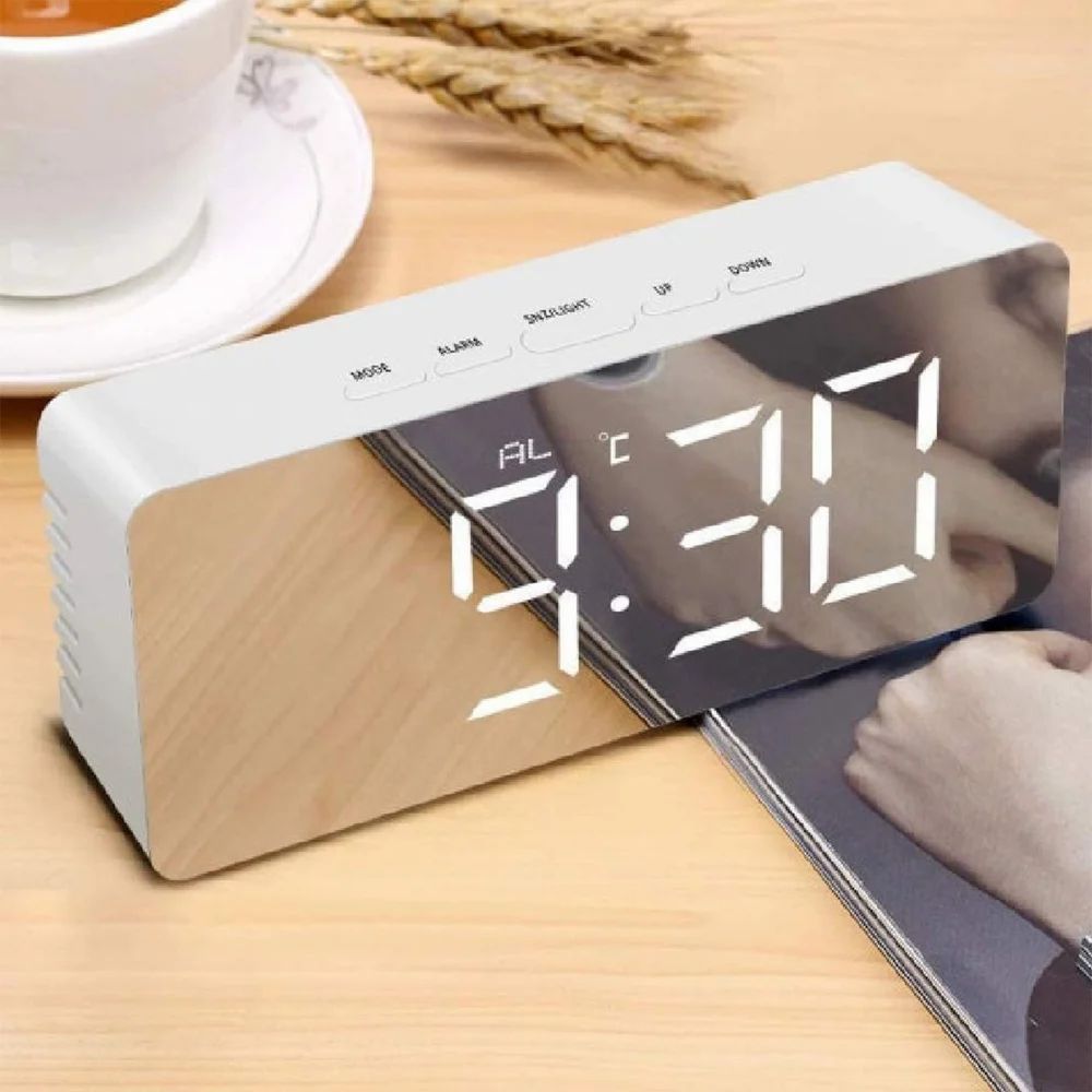 Digital clock on a wooden surface with a cup of coffee in the background